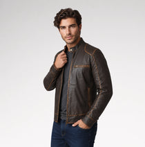 A man wearing a dark brown distressed leather motorcycle jacket over a gray t-shirt and blue jeans, standing against a light gray studio background.