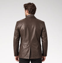 A man viewed from behind wearing a dark brown leather blazer over a collared shirt, set against a plain light gray studio background.