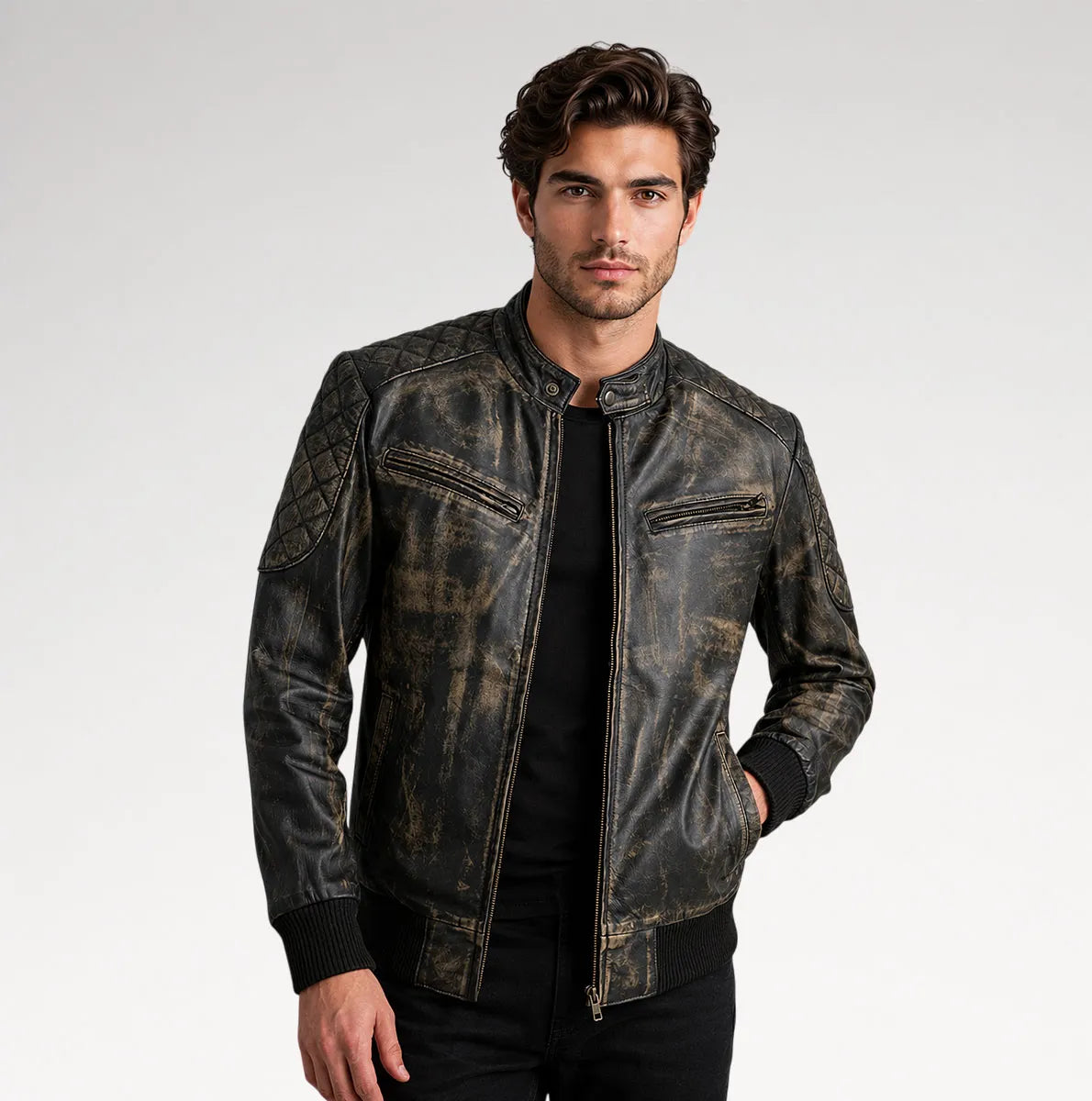A man wearing a distressed black leather jacket with a faded brown wash, styled over a black shirt and black pants, photographed against a light gray studio background.