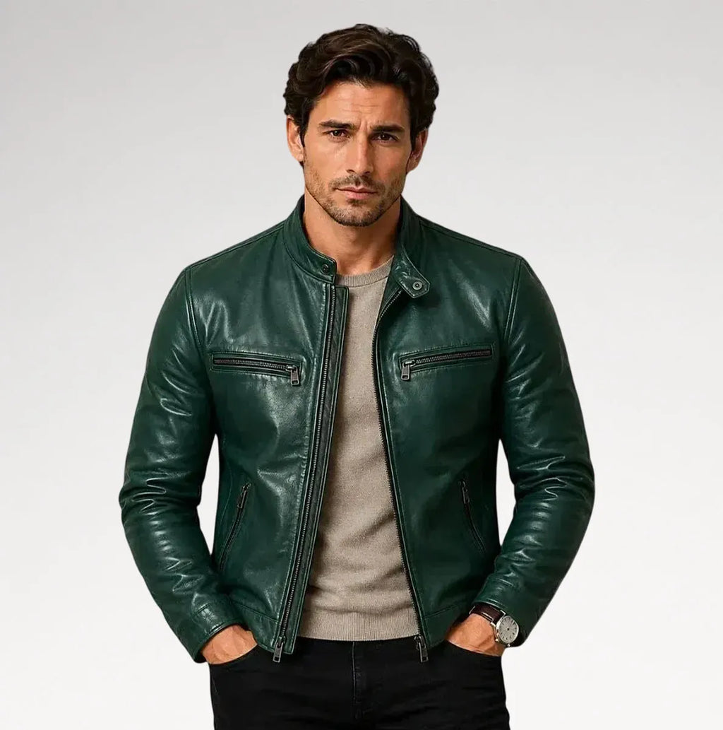 A man wearing a dark green leather jacket over a light gray crewneck sweater and black pants, standing against a light gray studio background.