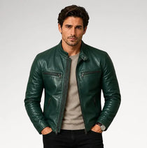 A man wearing a dark green leather jacket over a light gray crewneck sweater and black pants, standing against a light gray studio background.