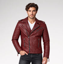 A man wearing a burgundy leather motorcycle jacket with quilted panels and silver zippers, styled over a white t-shirt and dark gray jeans, against a light gray studio background.