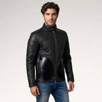 A man wearing a black quilted leather jacket with a high collar and front zipper, paired with blue jeans, photographed against a light gray studio background.