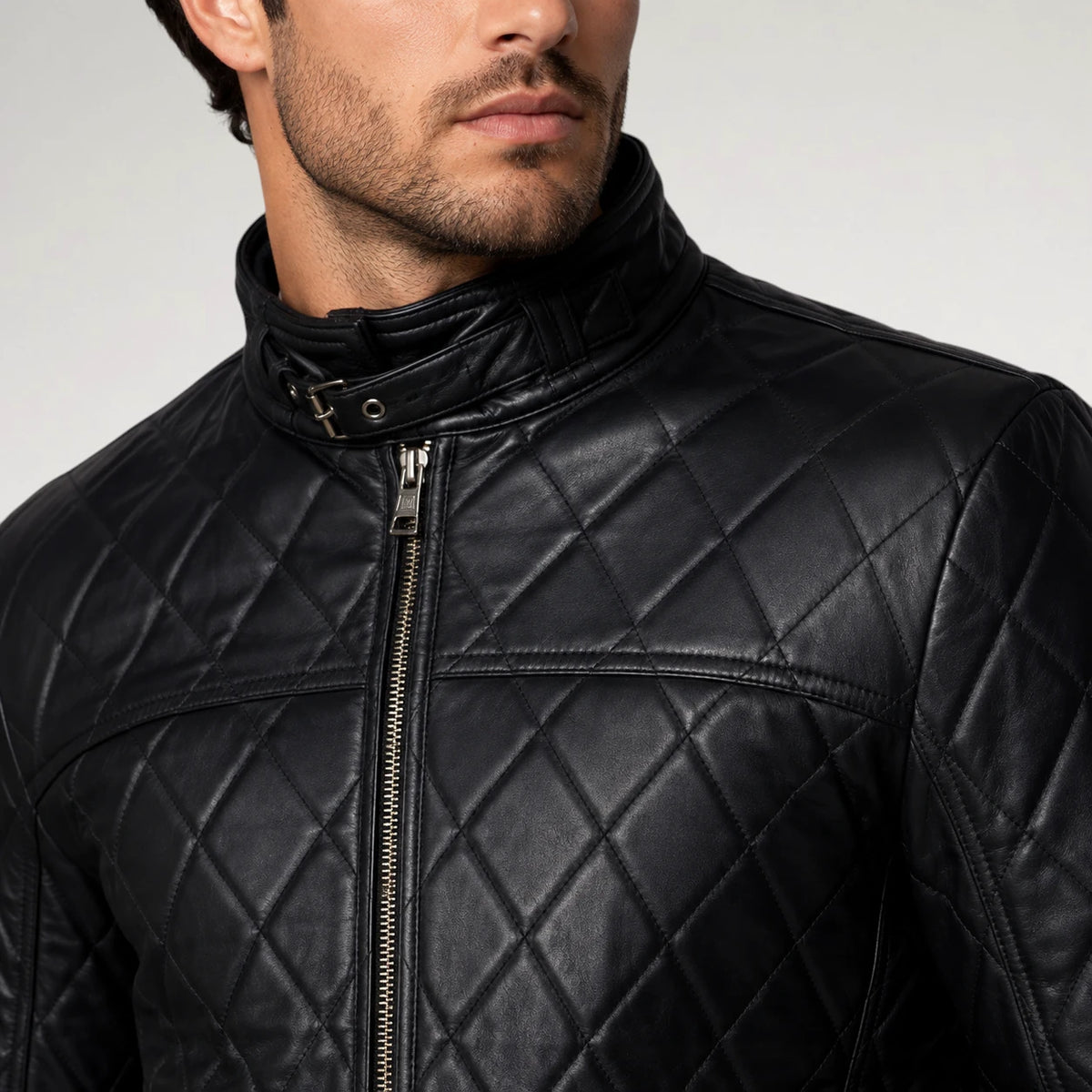 Close-up of a man wearing a black quilted leather jacket with a high stand-up collar and front zipper, against a light gray studio background.