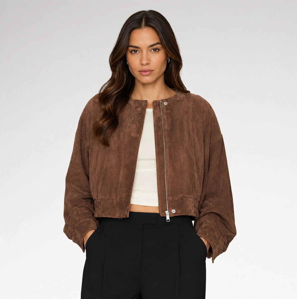 A woman modeling a cropped brown suede jacket with a front zipper, paired with a white crop top and black trousers, against a light gray studio background. Main image