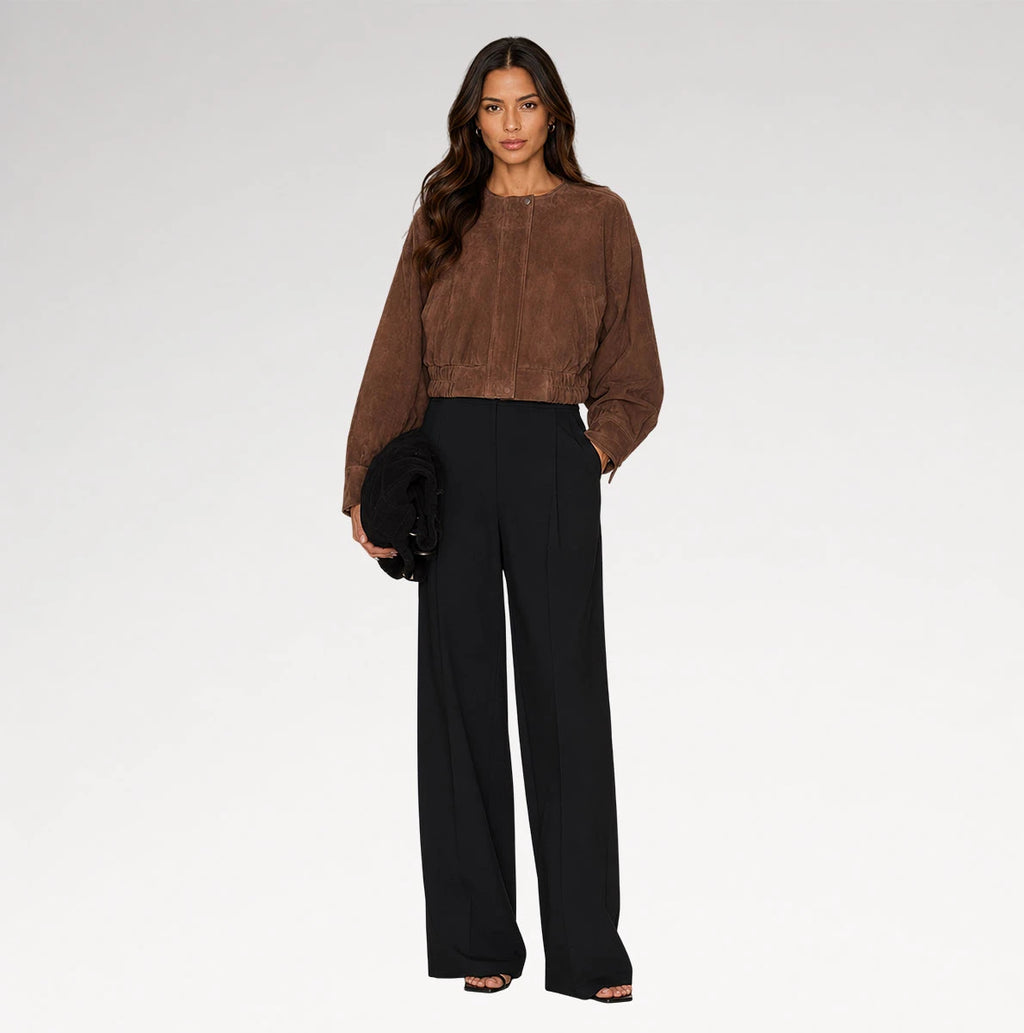 A woman modeling a brown cropped suede-like long-sleeve top and black wide-leg trousers against a light gray studio background.