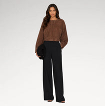 A woman modeling a brown cropped suede-like long-sleeve top and black wide-leg trousers against a light gray studio background.