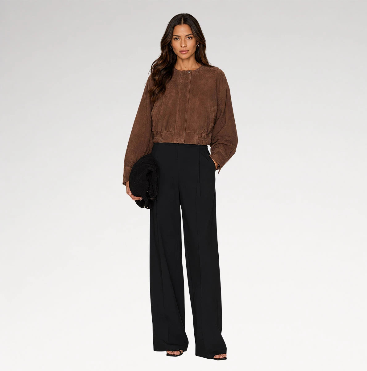 A woman modeling a brown cropped suede-like long-sleeve top and black wide-leg trousers against a light gray studio background.