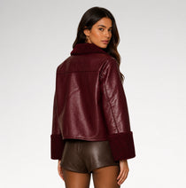 A woman shown from the back wearing a cropped, pebbled faux-leather jacket in deep burgundy with a matching faux-fur collar and cuffs, paired with brown faux-leather shorts, against a light gray studio background.