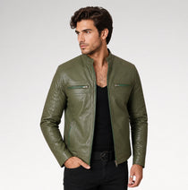 A man wearing an olive green leather jacket over a black shirt and black pants, standing against a light gray studio background.