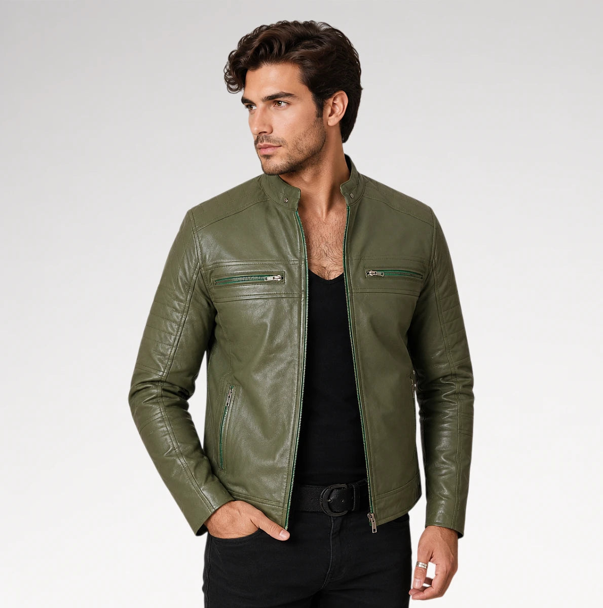 A man wearing an olive green leather jacket over a black shirt and black pants, standing against a light gray studio background.