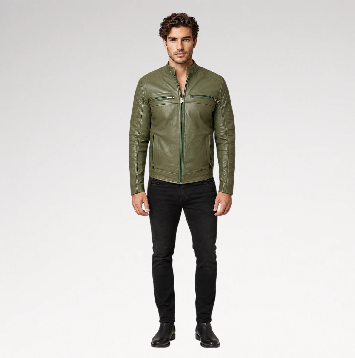 A man modeling an olive green leather jacket with black pants and black boots, standing against a light gray studio background.