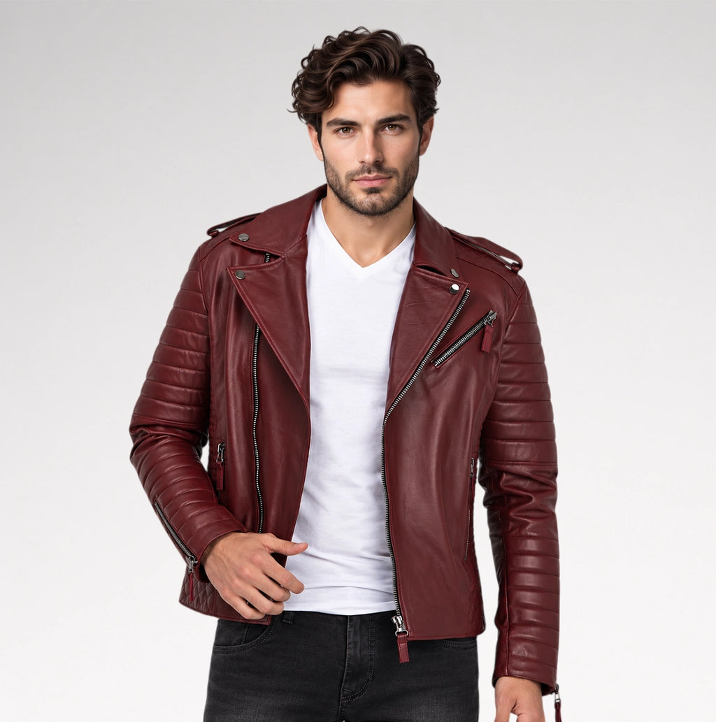 A man wearing a burgundy leather motorcycle jacket with quilted sleeves and diagonal zippers, layered over a white t-shirt and dark jeans, against a light gray studio background.