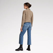 A woman shown from the back wearing a taupe suede cropped jacket, blue jeans, and black boots against a light gray studio background.