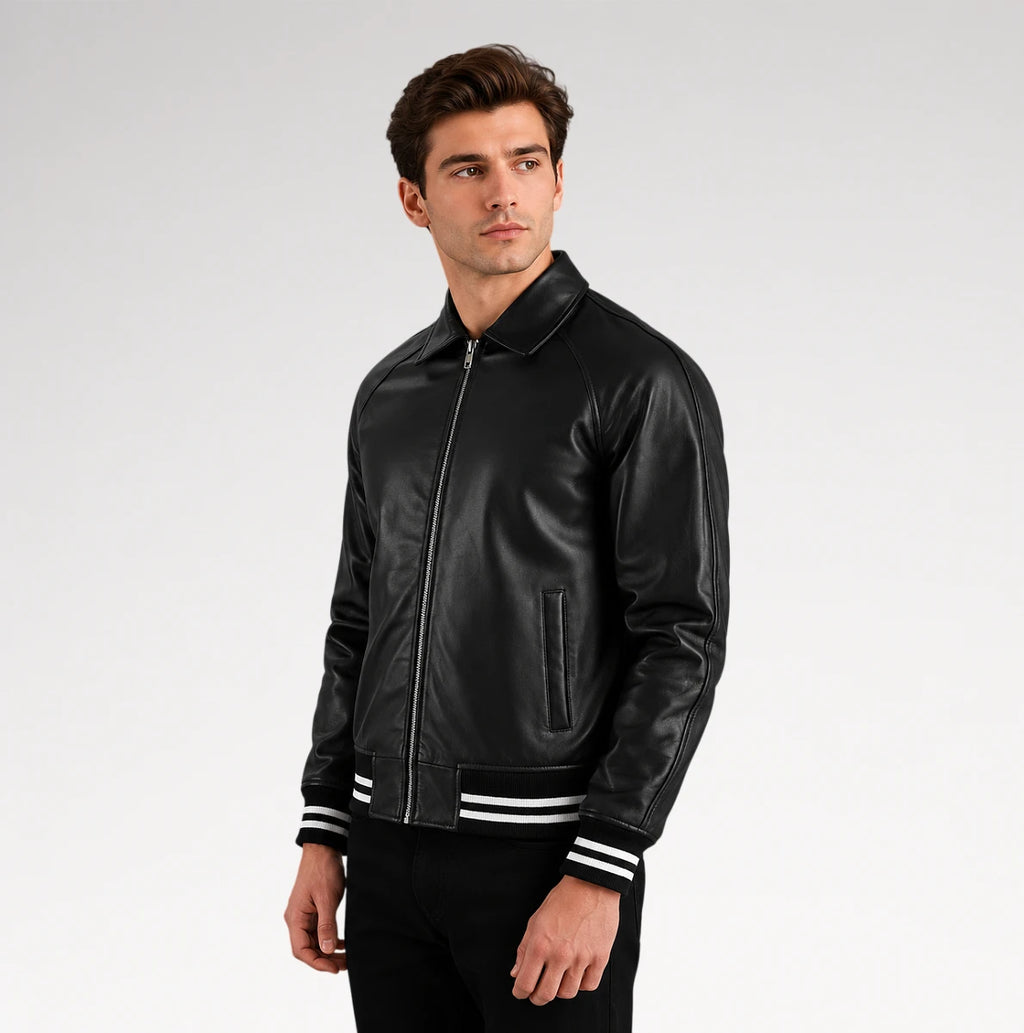 A man wearing a black leather bomber jacket with white stripes on the cuffs, posed against a light gray studio background.
