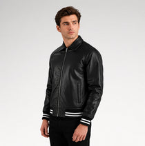 A man wearing a black leather bomber jacket with white stripes on the cuffs, posed against a light gray studio background.