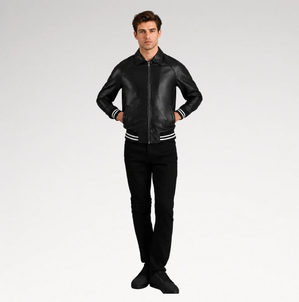 A man modeling a black leather bomber jacket with white stripe details on the cuffs and hem, paired with black pants and black sneakers, against a light gray studio background.