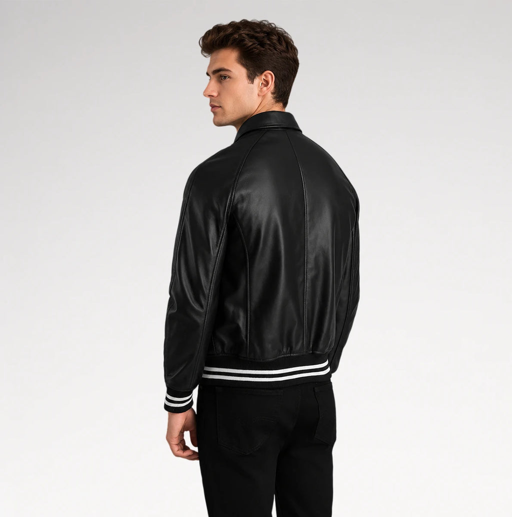 A man wearing a black leather bomber jacket with white stripe details on the cuffs and hem, shown from a side-back angle against a light gray studio background.