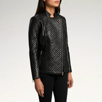 A woman wearing a black quilted faux-leather moto jacket with asymmetrical zipper details, shown from the waist up against a light gray studio background.