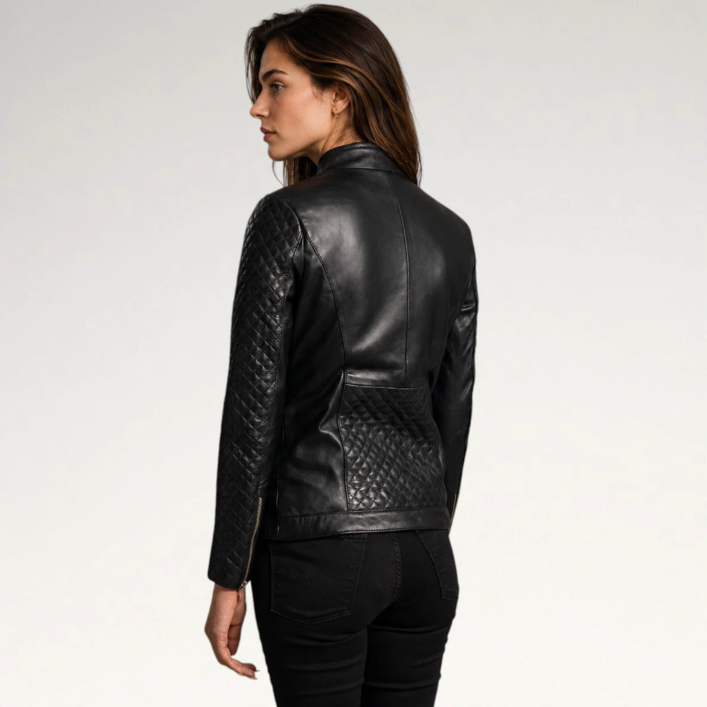 A woman shown from the back wearing a black leather jacket with quilted sleeve panels and a quilted back pocket, paired with black pants, against a plain light gray studio background.