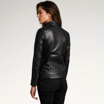 A woman shown from the back wearing a black leather jacket with quilted sleeve panels and a quilted back pocket, paired with black pants, against a plain light gray studio background.
