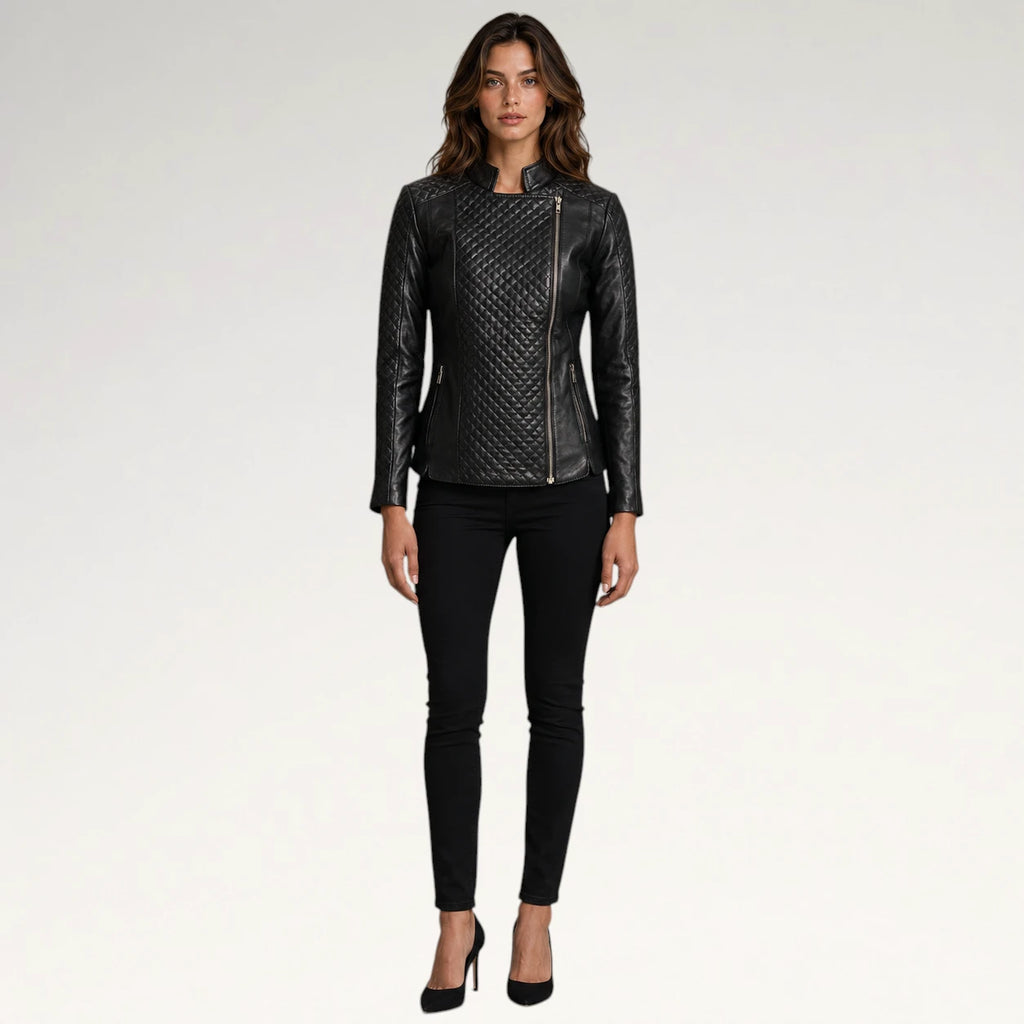 A woman modeling a black quilted faux-leather moto jacket with asymmetrical zipper details, paired with black skinny jeans and black high heels, against a plain light gray studio background.