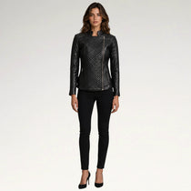 A woman modeling a black quilted faux-leather moto jacket with asymmetrical zipper details, paired with black skinny jeans and black high heels, against a plain light gray studio background.