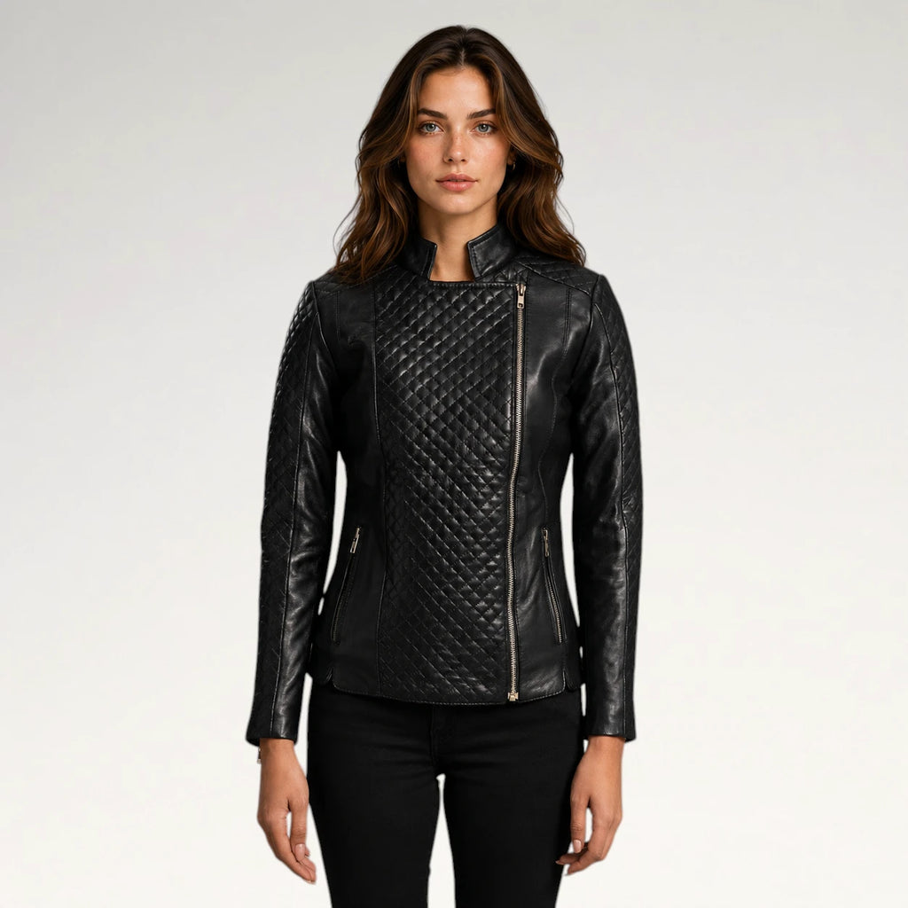 A woman modeling a black quilted faux-leather moto jacket with asymmetrical zipper details, photographed against a plain light gray studio background.