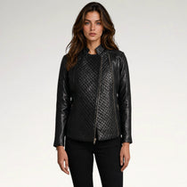A woman modeling a black faux-leather moto jacket with quilted diamond-patterned front panels and smooth leather sleeves, paired with black pants, against a light gray studio background.