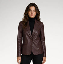 A woman modeling a dark brown faux-leather blazer over a black turtleneck sweater and black pants, photographed against a neutral light gray studio background.