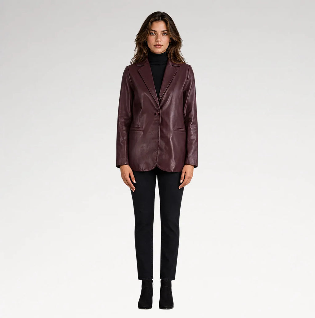A woman modeling a dark burgundy leather blazer over a black turtleneck, paired with black pants and black ankle boots, against a light gray studio background.