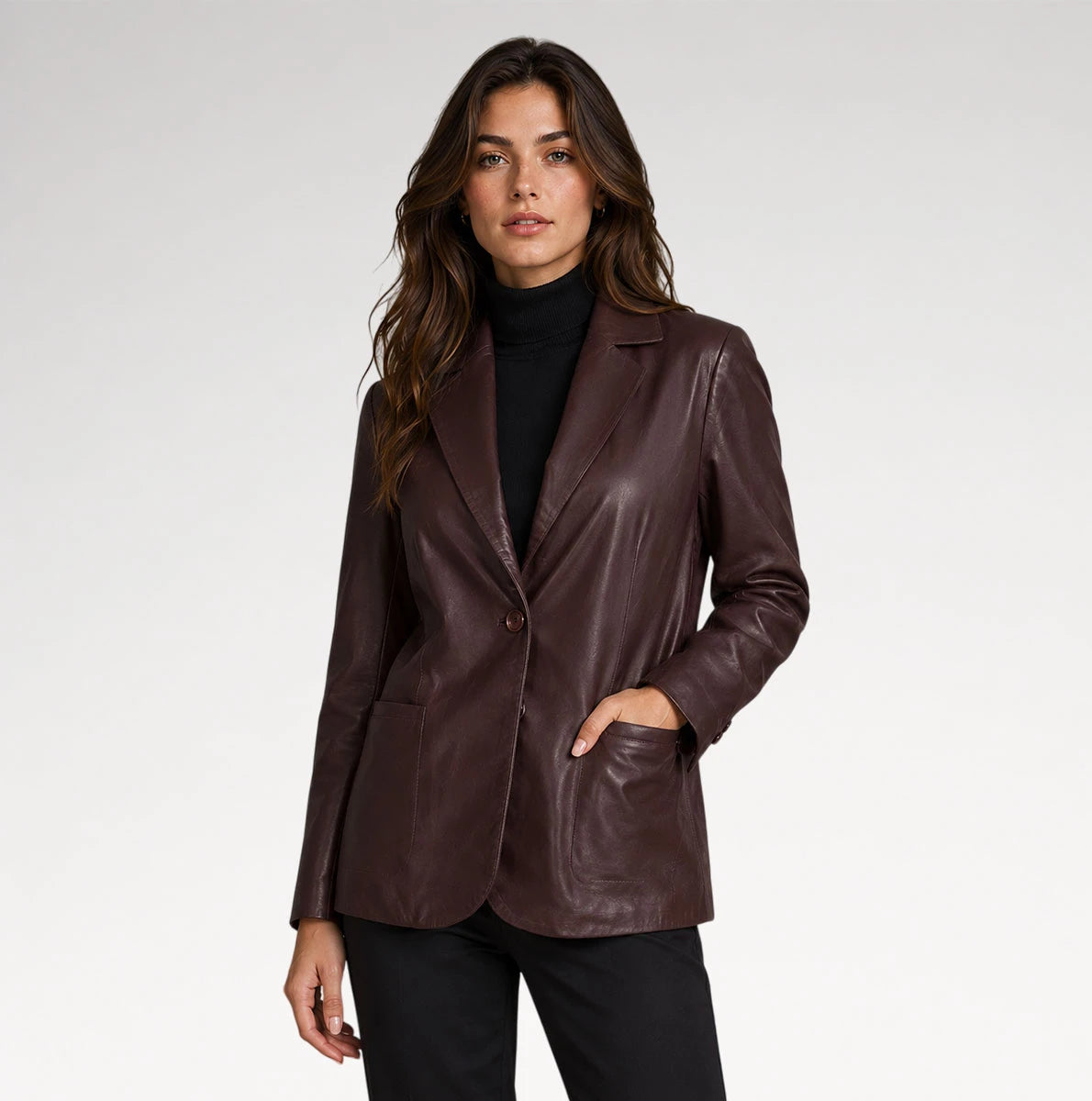 A woman modeling a dark brown faux-leather blazer over a black turtleneck and black pants, photographed against a light gray studio background.