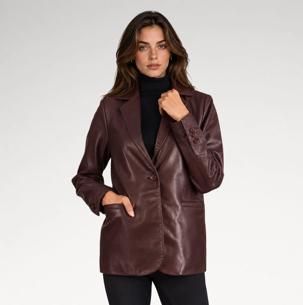 A woman modeling a dark brown faux-leather blazer over a black turtleneck sweater, set against a plain light gray studio background.