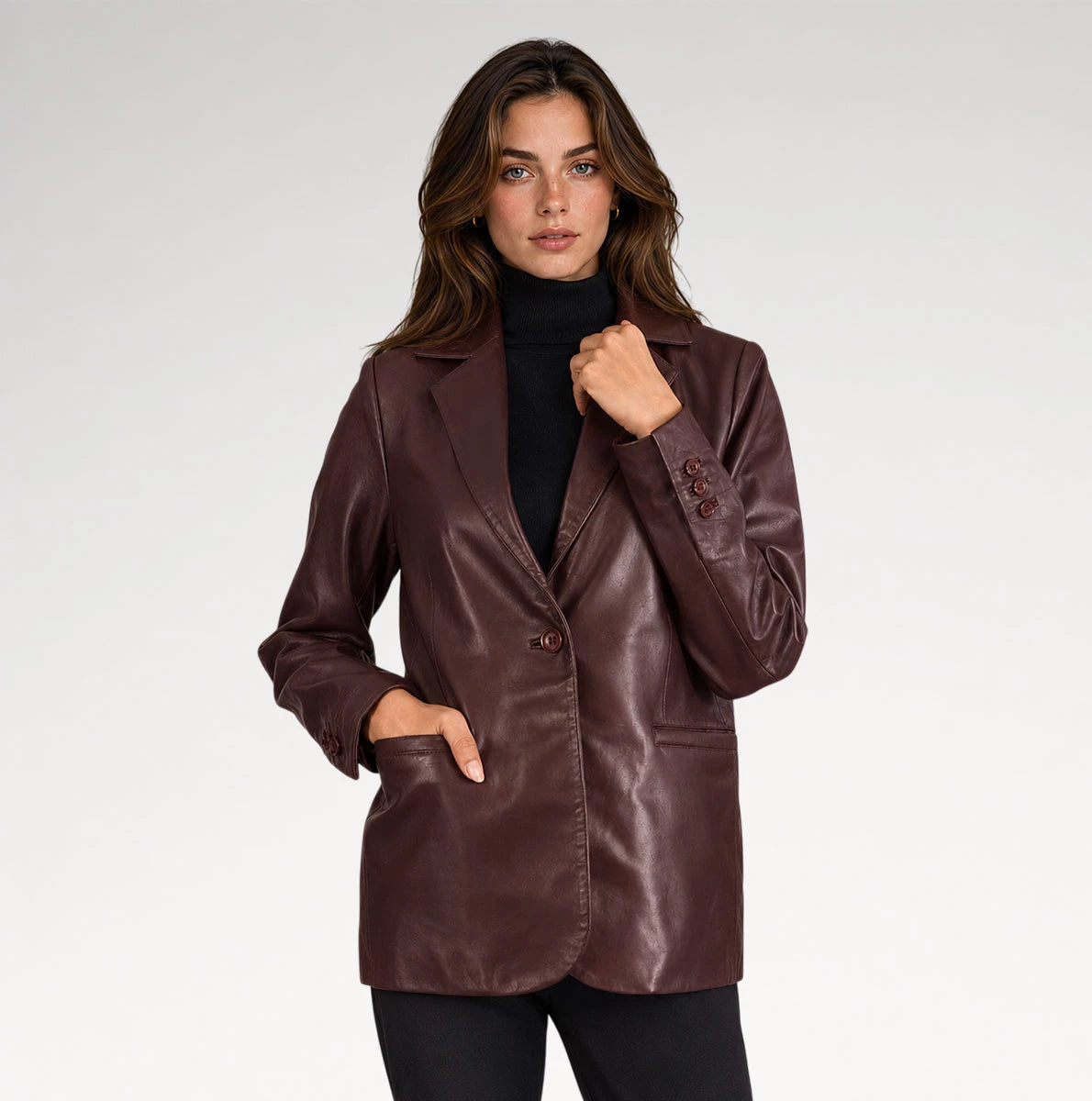 A woman modeling a dark brown faux-leather blazer over a black turtleneck sweater, set against a plain light gray studio background.