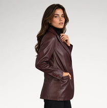 A woman wearing a dark brown leather blazer over a black turtleneck, photographed against a light gray studio background.