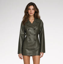 A woman modeling a dark olive green faux leather double-breasted blazer and matching mini skirt against a light gray studio background.