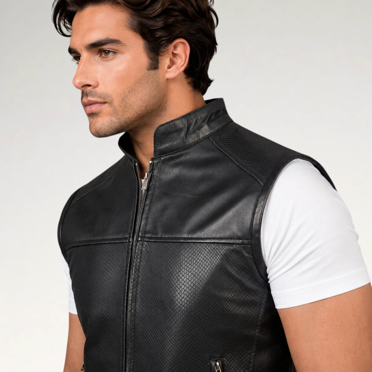A man wearing a black leather vest over a white t-shirt, shown in a close-up profile shot against a light gray studio background.