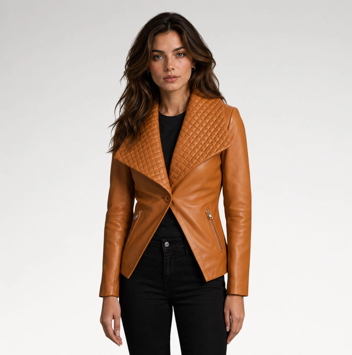 A woman modeling a tan leather moto jacket with a quilted asymmetrical yoke and silver zippers, paired with a black top and black jeans, against a light gray studio background.