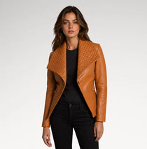 A woman modeling a tan leather jacket with a quilted wrap-style collar, worn over a black top and black jeans, against a light gray studio background.