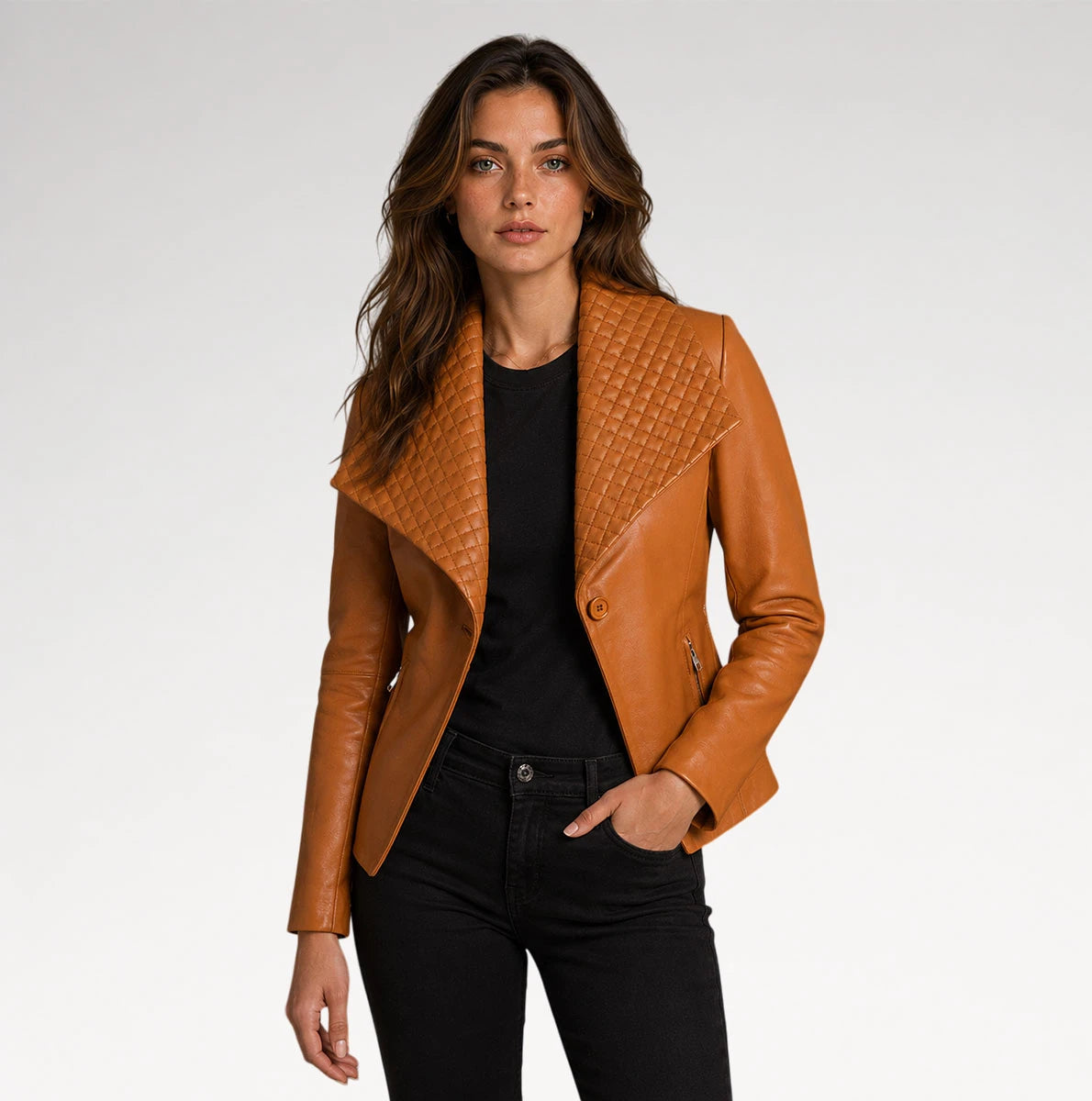 A woman modeling a tan leather moto jacket with a quilted yoke and asymmetrical collar, worn over a black top and black jeans against a light gray studio background.