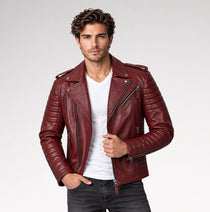 A man wearing a burgundy leather moto jacket over a white t-shirt and dark jeans, standing against a light gray studio background.