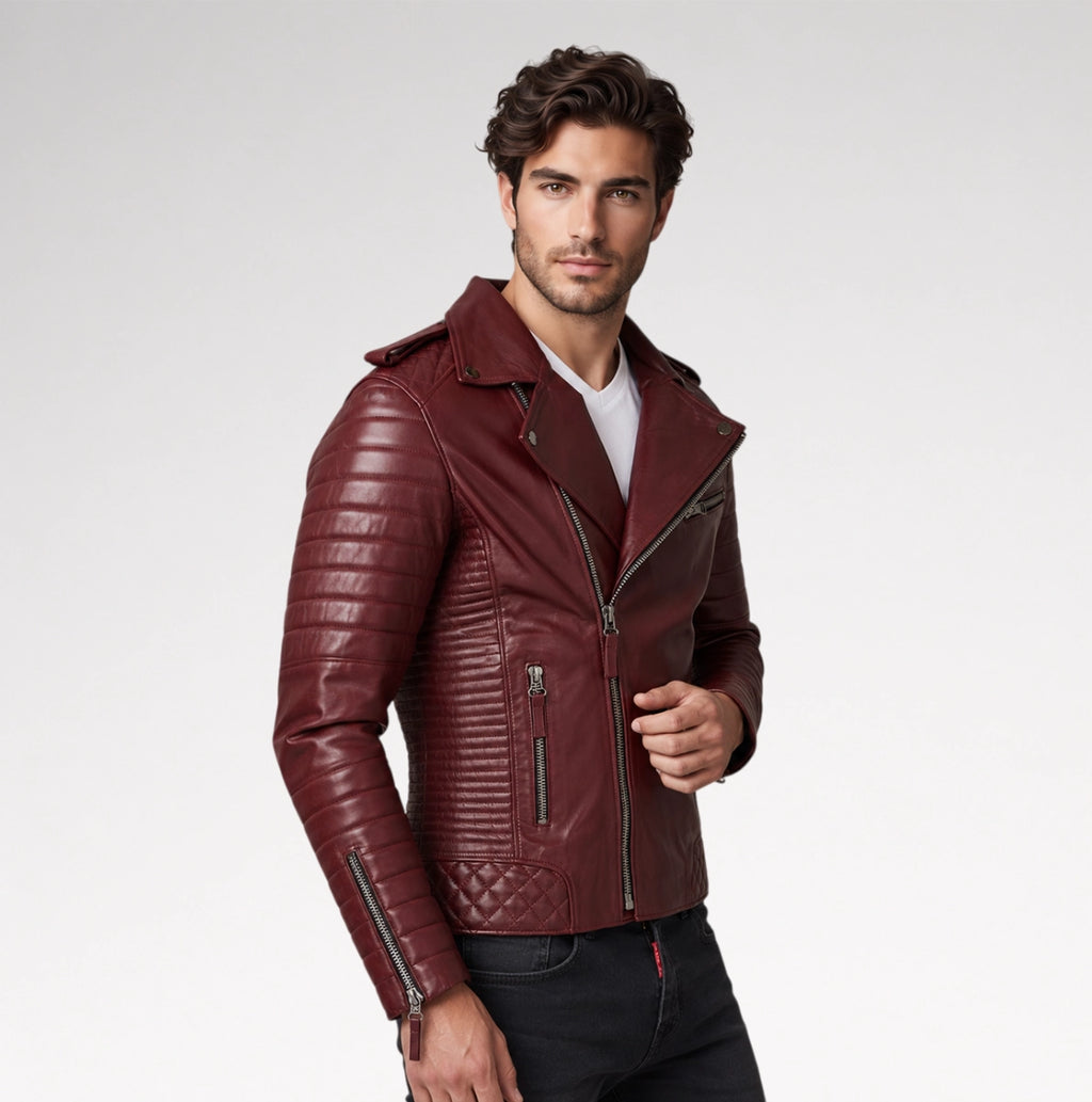 A man wearing a burgundy faux leather motorcycle jacket with quilted and zippered details, styled over a white t-shirt and dark jeans, photographed against a light gray studio background.