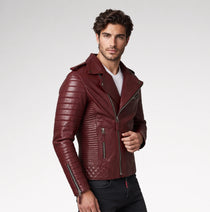 A man wearing a burgundy faux leather motorcycle jacket with quilted and zippered details, styled over a white t-shirt and dark jeans, photographed against a light gray studio background.