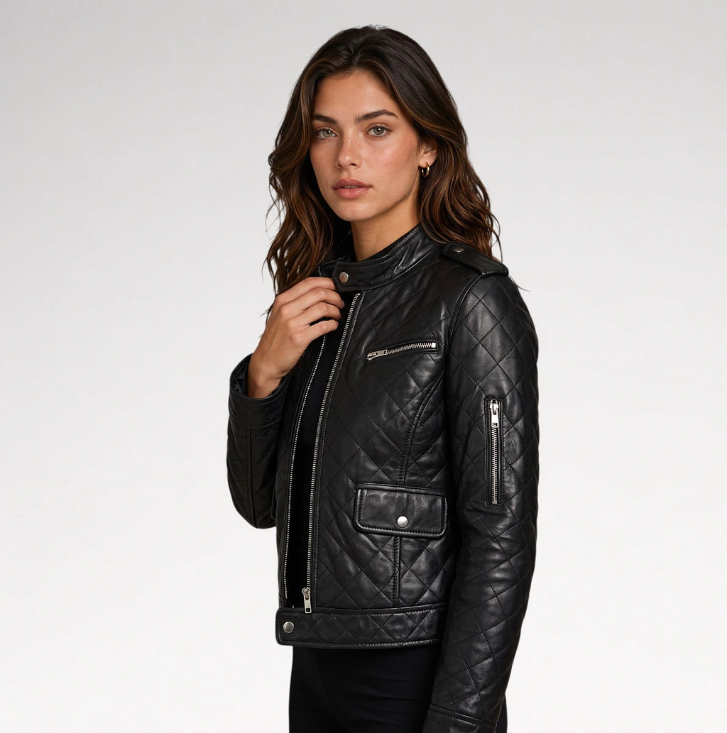 A woman wearing a black quilted leather moto jacket with silver zippers, photographed against a clean light gray studio background.