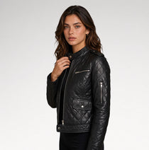 A woman wearing a black quilted leather moto jacket with silver zippers, photographed against a clean light gray studio background.