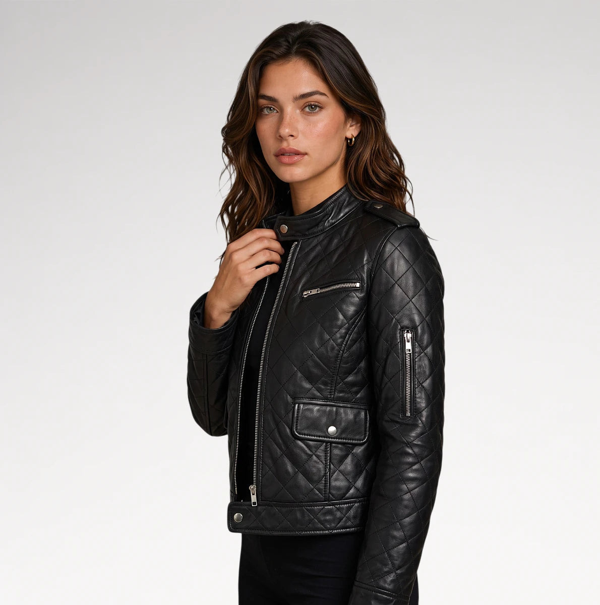 A woman wearing a black quilted leather moto jacket with silver zippers, photographed against a clean light gray studio background.
