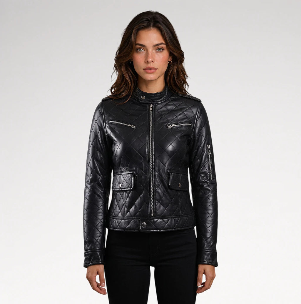 A woman modeling a black quilted faux-leather moto jacket with silver zippers and flap pockets, paired with black pants, against a light gray studio background.