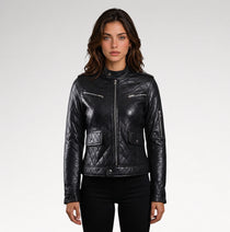 A woman modeling a black quilted faux-leather moto jacket with silver zippers and flap pockets, paired with black pants, against a light gray studio background.