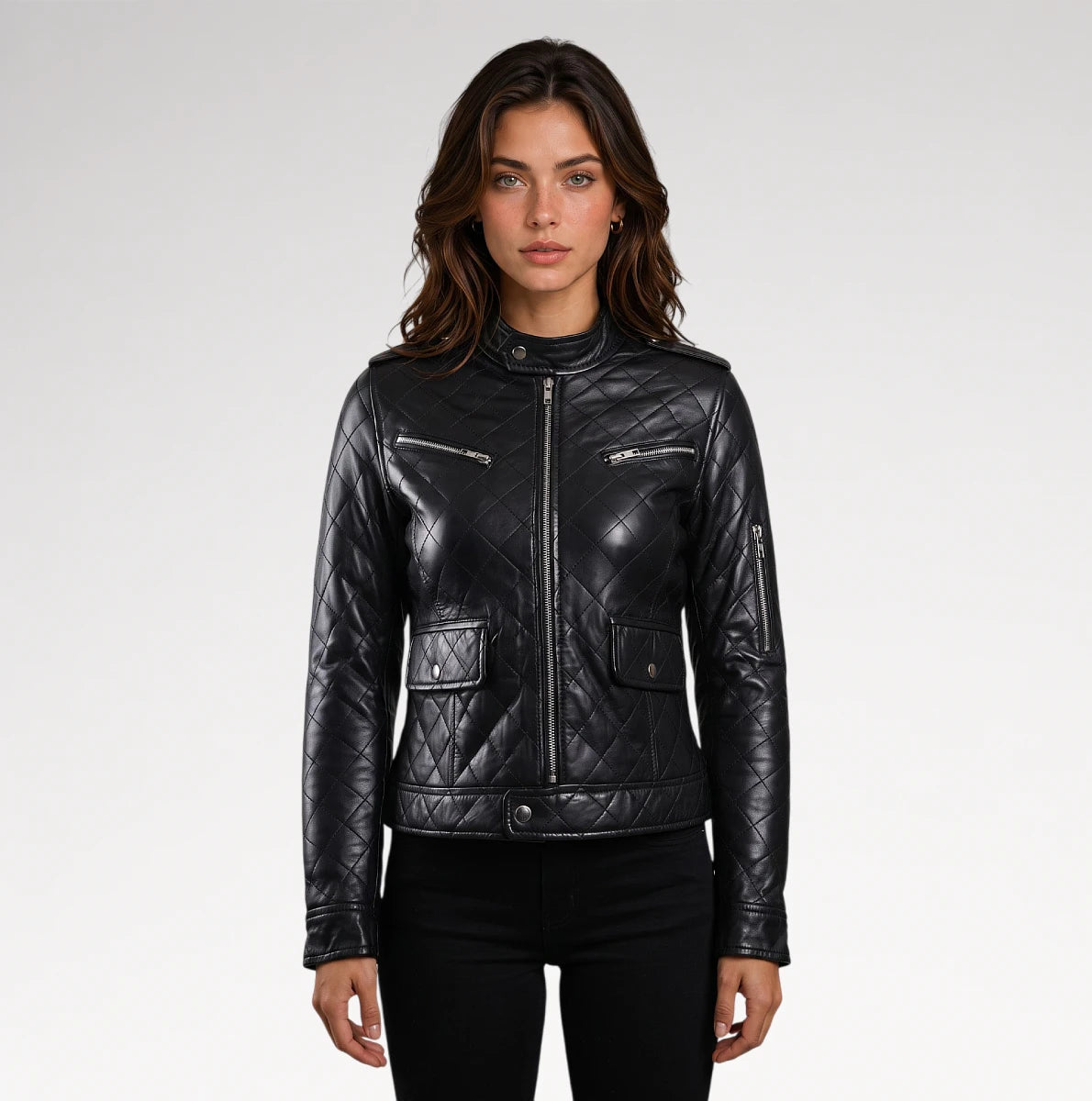 A woman modeling a black quilted faux-leather moto jacket with silver zippers and flap pockets, paired with black pants, against a light gray studio background.