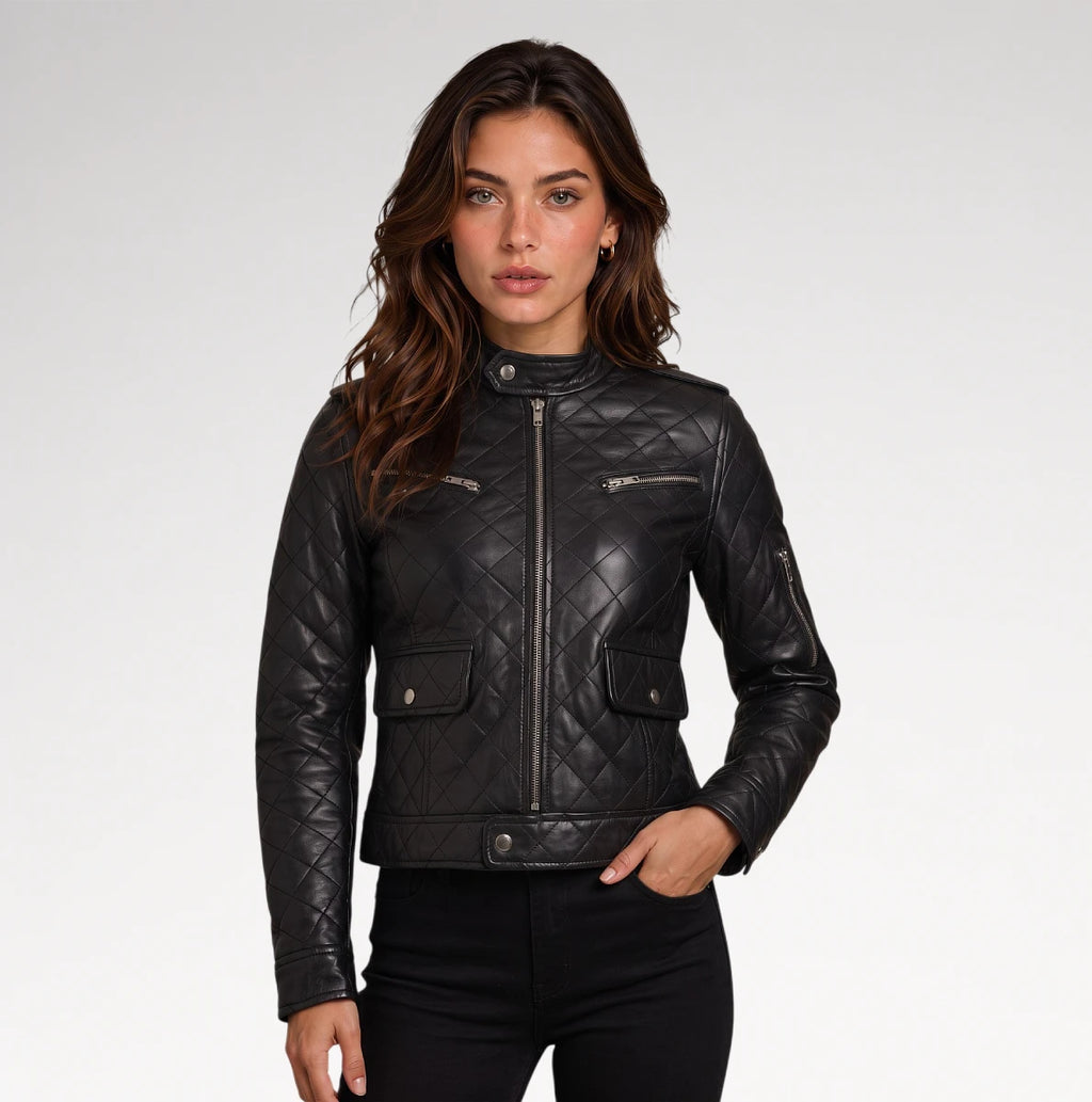 A woman wearing a black quilted faux-leather moto jacket with silver zippers, paired with black pants, photographed against a light gray studio background.